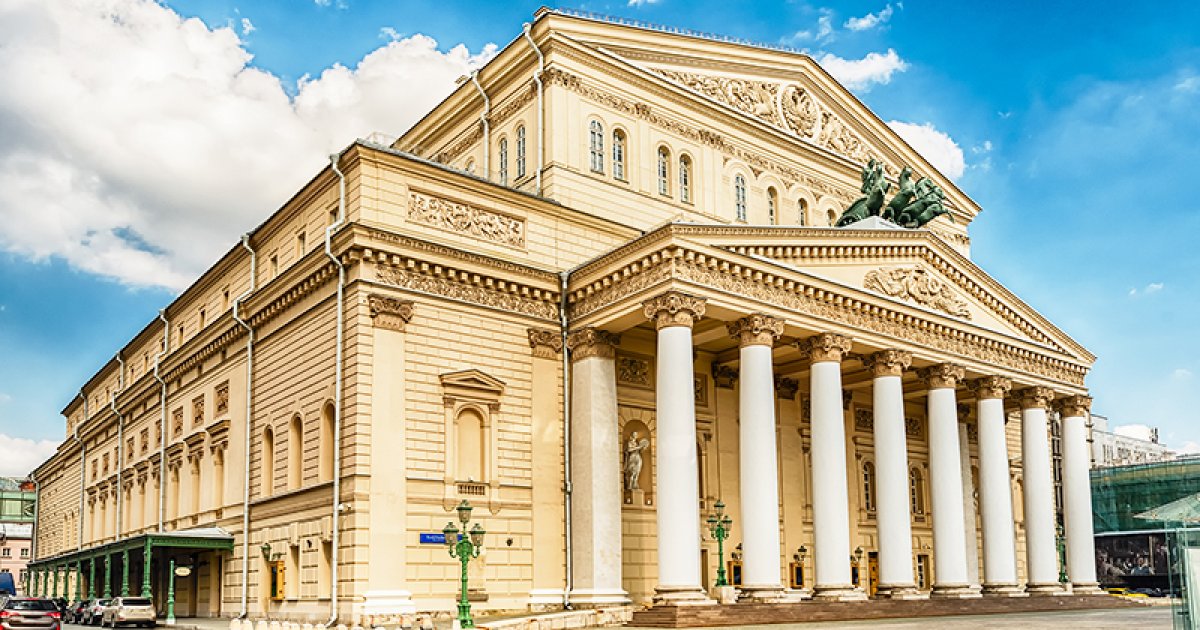 Wide view of the Bolshoi stage with an opulent red curtain and ornate proscenium framing the performance space