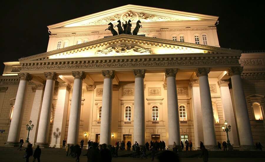 Facade of the Bolshoi Theatre in Moscow at dusk with illuminated portico and classical sculptures