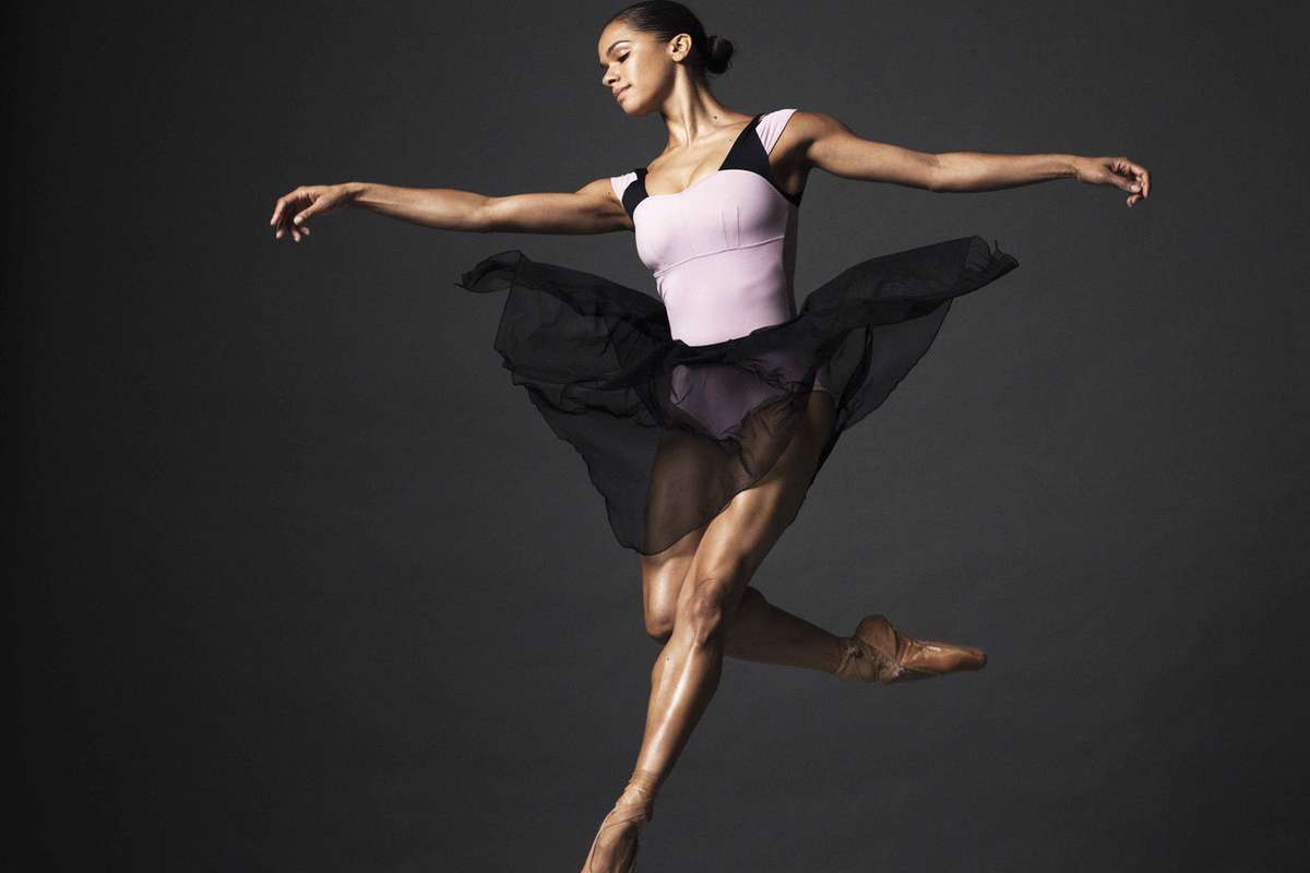 Misty Copeland mid-performance center stage, poised in an arabesque with focused expression and dramatic lighting
