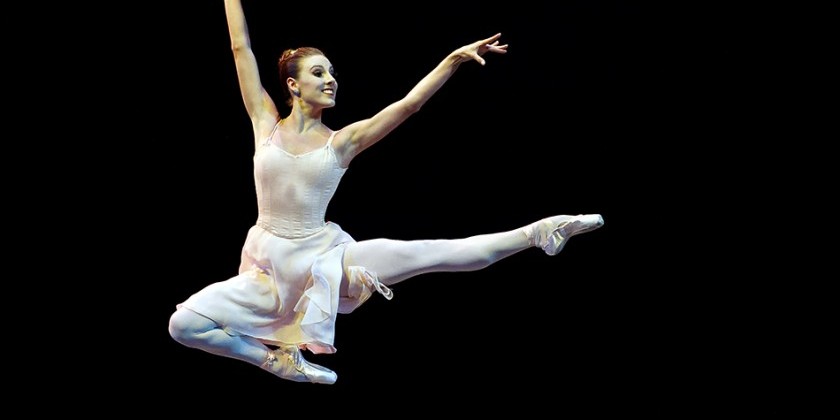 Tiler Peck on stage with arms extended in a crisp Balanchine pose, spotlight highlighting her precise line